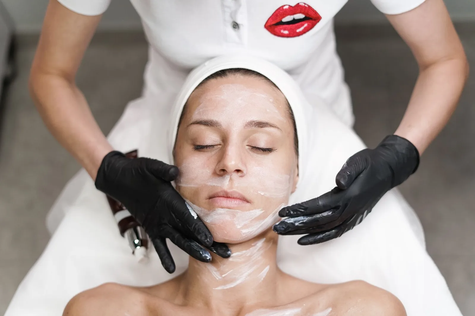 Una esteticista con guantes negros hace un facial a una clienta