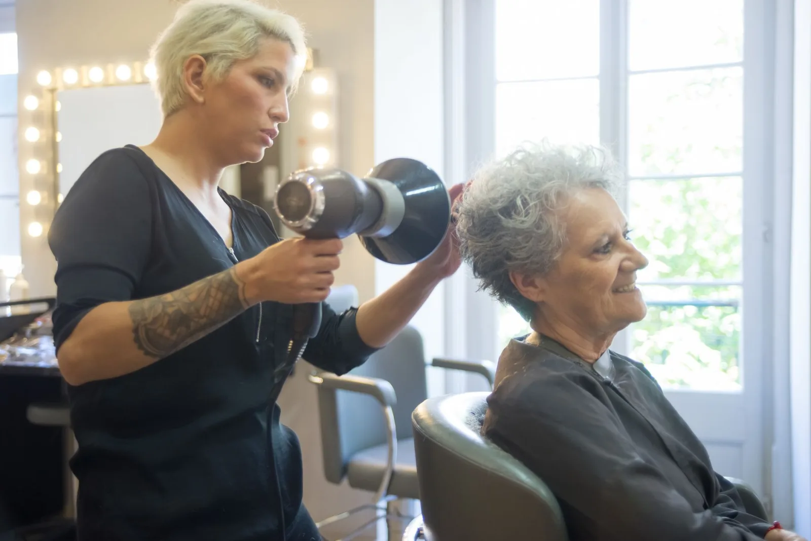 Una parrucchiera asciuga i capelli a una cliente anziana
